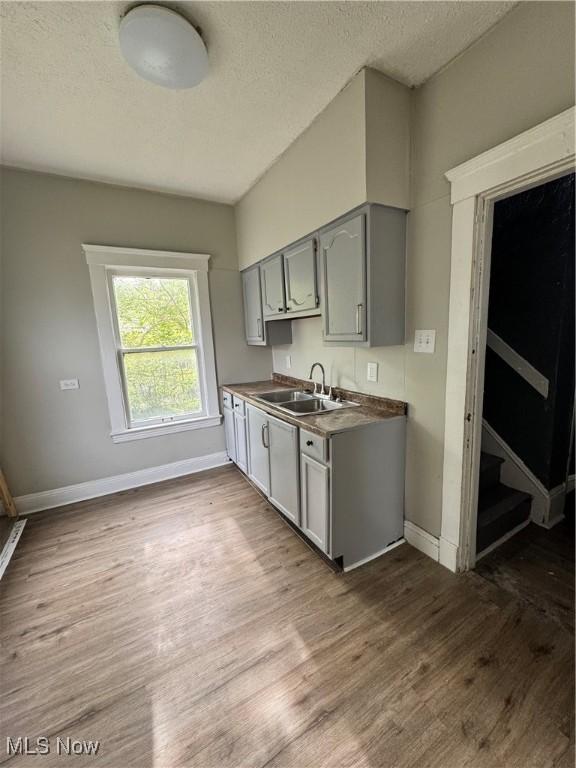 483 E 128th St, Cleveland, OH 44108 - kitchen with gray cabinetry, a sink, a textured ceiling, baseboards, and wood finished floors