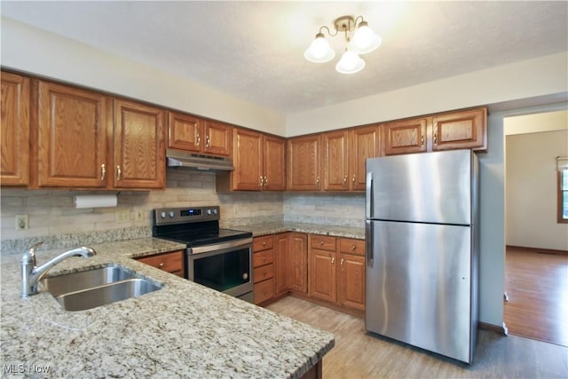 28420 Glen Hollow Ln, Olmsted Falls, OH 44138 - kitchen with stainless steel appliances, under cabinet range hood, brown cabinetry, a sink, and light stone counters
