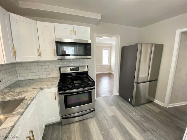 4485 Baintree Rd, University Heights, OH 44118 - kitchen with appliances with stainless steel finishes, light stone counters, wood finished floors, white cabinetry, and decorative backsplash