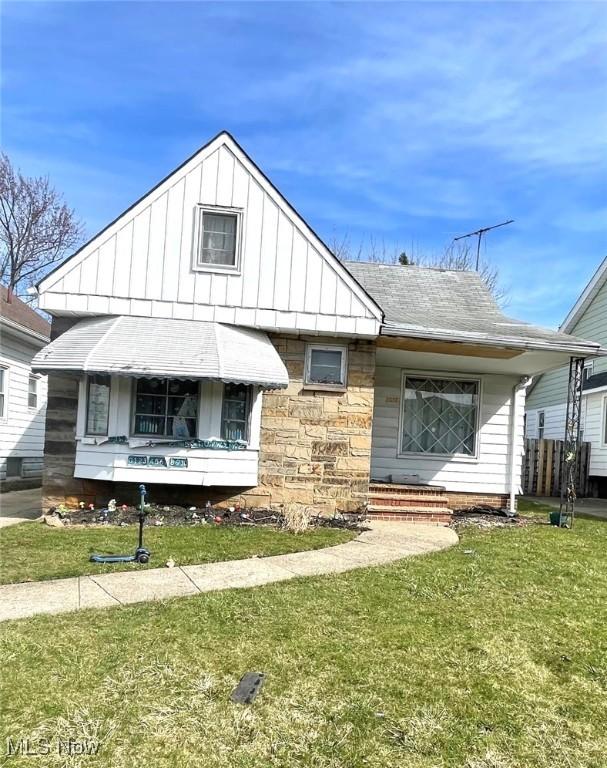 4815 E 86th St, Garfield Heights, OH 44125 - view of front of property featuring board and batten siding, a front lawn, roof with shingles, and stone siding