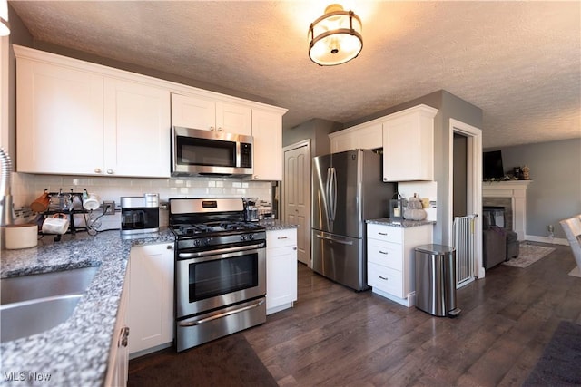 10957 Mogadore Ave NW, Uniontown, OH 44685 - kitchen with appliances with stainless steel finishes, dark wood-type flooring, white cabinets, decorative backsplash, and light stone countertops