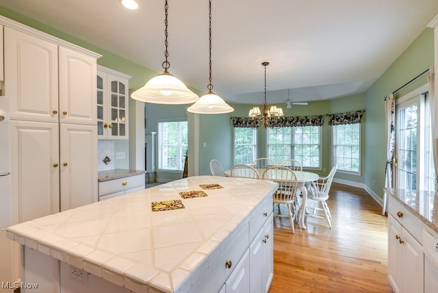 835 Thelma Dr, Wadsworth, OH 44281 - kitchen with tile countertops, light wood-style floors, white cabinetry, glass insert cabinets, and pendant lighting