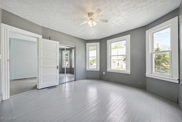 3399 E 65th St, Cleveland, OH 44127 - unfurnished bedroom featuring a textured ceiling, multiple windows, hardwood / wood-style flooring, baseboards, and a ceiling fan