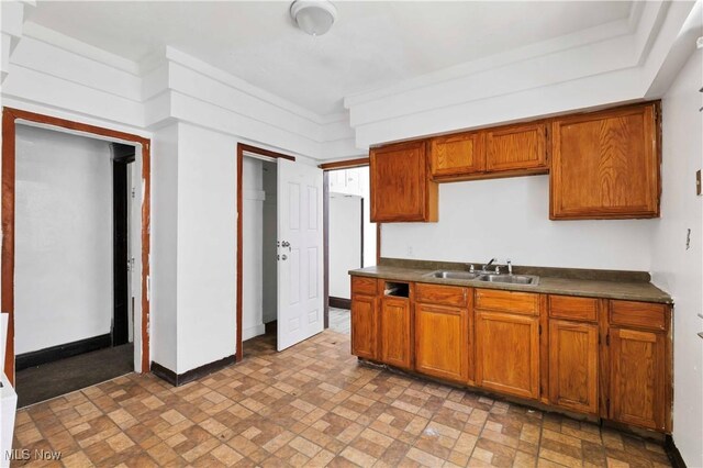 851 Paxton Rd, Cleveland, OH 44108 - kitchen with dark countertops, brick patterned floors, brown cabinetry, baseboards, and a sink