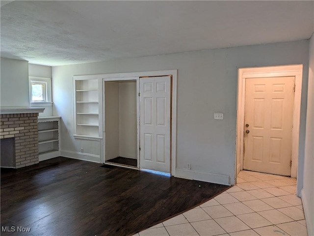 1367 Clearaire Rd, Cleveland, OH 44110 - unfurnished living room featuring built in shelves, wood finished floors, a brick fireplace, and baseboards