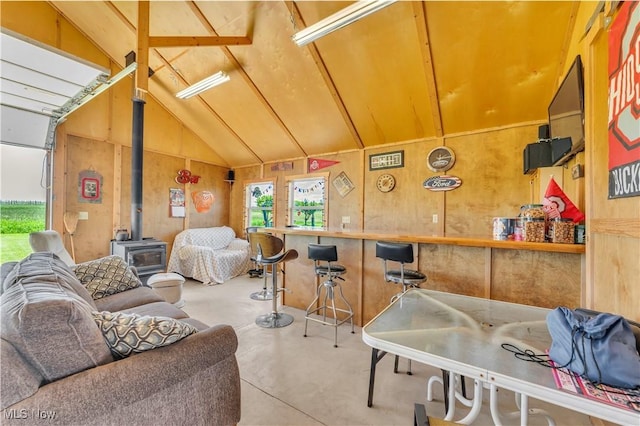 9903 Vermilion Rd, Amherst, OH 44001 - living area featuring a wood stove, concrete floors, plenty of natural light, vaulted ceiling, and wood walls