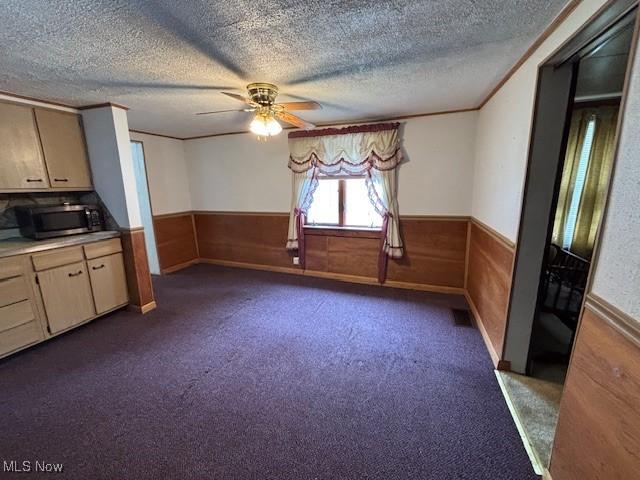 1445 E County Line Rd, Mineral Ridge, OH 44440 - unfurnished dining area featuring wainscoting, ceiling fan, dark colored carpet, a textured ceiling, and wooden walls