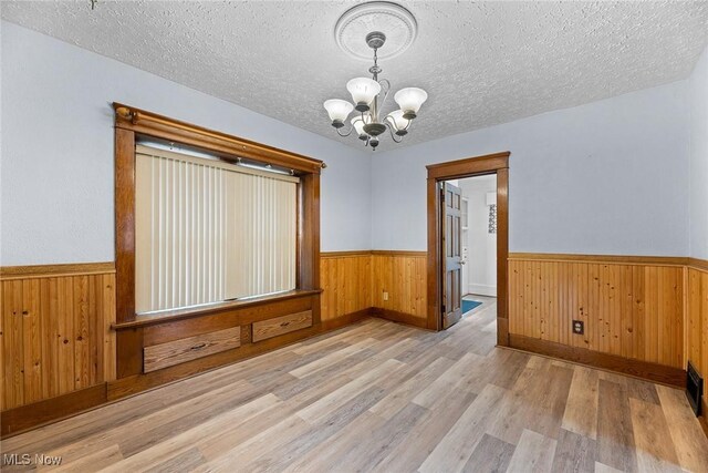 916 Kling St, Akron, OH 44311 - spare room with a chandelier, a wainscoted wall, wood finished floors, wood walls, and a textured ceiling