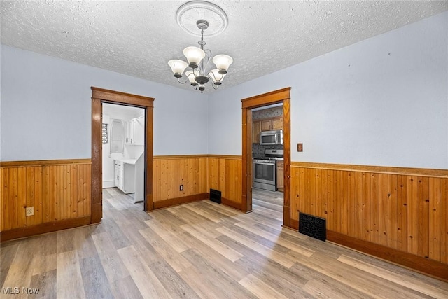 916 Kling St, Akron, OH 44311 - spare room featuring wainscoting, a chandelier, light wood-style flooring, wooden walls, and a textured ceiling