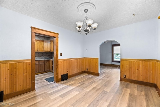 916 Kling St, Akron, OH 44311 - unfurnished dining area with a wainscoted wall, arched walkways, a chandelier, light wood-type flooring, and wooden walls
