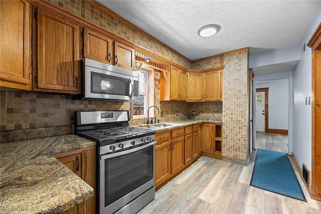 916 Kling St, Akron, OH 44311 - kitchen with appliances with stainless steel finishes, a sink, light wood-style flooring, brown cabinetry, and tasteful backsplash