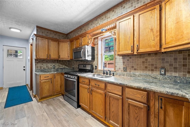 916 Kling St, Akron, OH 44311 - kitchen featuring appliances with stainless steel finishes, brown cabinetry, a textured ceiling, light wood finished floors, and a sink