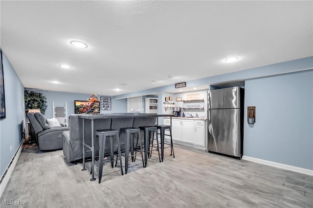 5512 Berkshire Dr, North Olmsted, OH 44070 - kitchen featuring freestanding refrigerator, light wood-style floors, white cabinetry, a breakfast bar, and baseboards