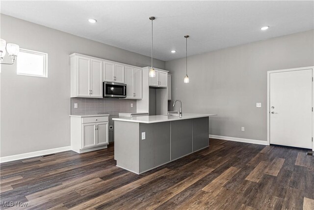 360 Bascule Dr, Lorain, OH 44052 - kitchen featuring stainless steel microwave, dark wood-style flooring, white cabinetry, decorative backsplash, and a center island with sink