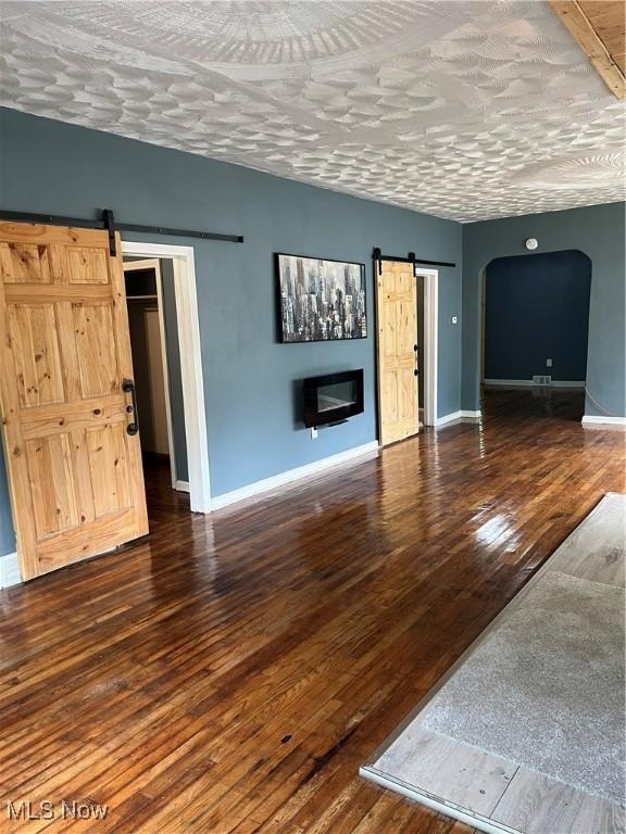 1264 Diagonal Rd, Akron, OH 44307 - unfurnished living room with a barn door, arched walkways, baseboards, and wood finished floors