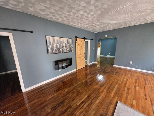 1264 Diagonal Rd, Akron, OH 44307 - unfurnished living room featuring a barn door, hardwood / wood-style floors, baseboards, a textured ceiling, and arched walkways