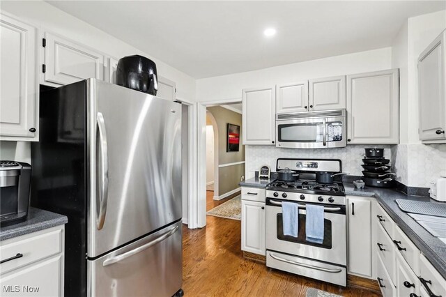 3945 Meadowbrook Blvd, University Heights, OH 44118 - kitchen with appliances with stainless steel finishes, dark countertops, arched walkways, wood finished floors, and white cabinetry