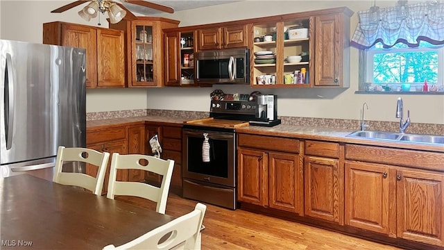5981 Westfall St SE, Waynesburg, OH 44688 - kitchen with stainless steel appliances, a sink, brown cabinetry, a ceiling fan, and glass insert cabinets