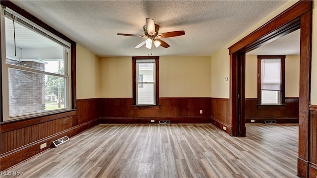 821 9th St SW, Massillon, OH 44647 - empty room featuring wood finished floors, a ceiling fan, plenty of natural light, wainscoting, and a textured ceiling