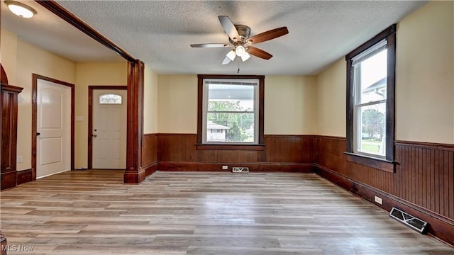 821 9th St SW, Massillon, OH 44647 - empty room featuring light wood-type flooring, healthy amount of natural light, wainscoting, a ceiling fan, and a textured ceiling