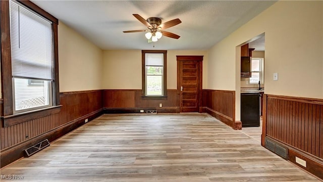 821 9th St SW, Massillon, OH 44647 - empty room featuring a wainscoted wall, light wood finished floors, ceiling fan, and wooden walls