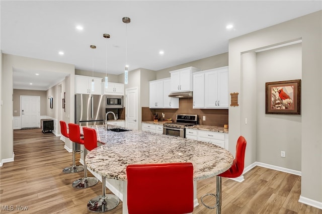 7834 Hunting Lake Dr, Concord, OH 44077 - kitchen with appliances with stainless steel finishes, a sink, under cabinet range hood, a kitchen bar, and light wood-style flooring