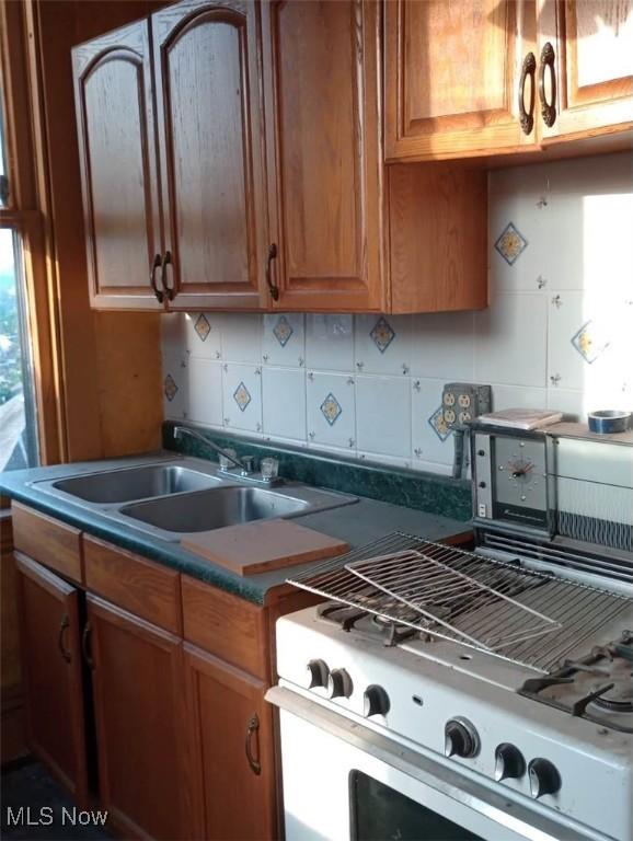 424 Elm St, Martins Ferry, OH 43935 - kitchen featuring white gas stove, a sink, brown cabinetry, and backsplash