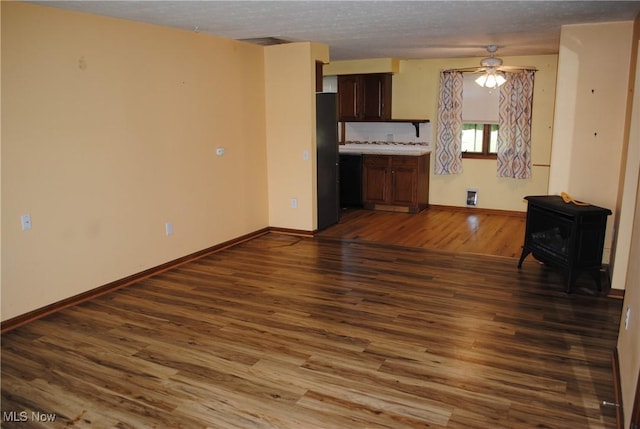13350 Baumhart Rd, Amherst, OH 44001 - unfurnished living room featuring a wood stove, a ceiling fan, dark wood-style floors, baseboards, and a textured ceiling