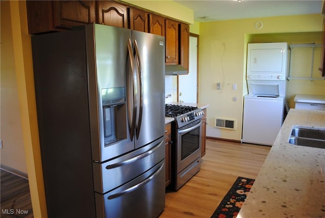 13350 Baumhart Rd, Amherst, OH 44001 - kitchen with appliances with stainless steel finishes, stacked washing machine and dryer, light wood-type flooring, a sink, and brown cabinetry
