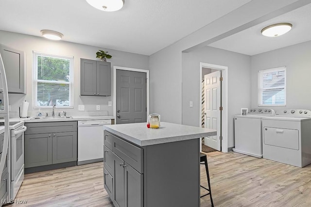 319 Sterling Ct, Akron, OH 44304 - kitchen featuring washer and clothes dryer, white appliances, gray cabinets, a kitchen bar, and light wood-type flooring