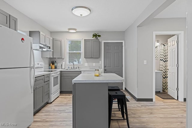319 Sterling Ct, Akron, OH 44304 - kitchen with white appliances, gray cabinets, under cabinet range hood, and a breakfast bar