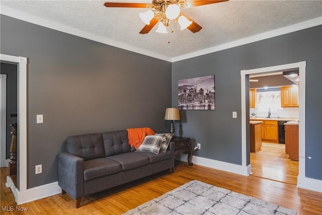 living area with light wood finished floors, ceiling fan, a textured ceiling, baseboards, and ornamental molding