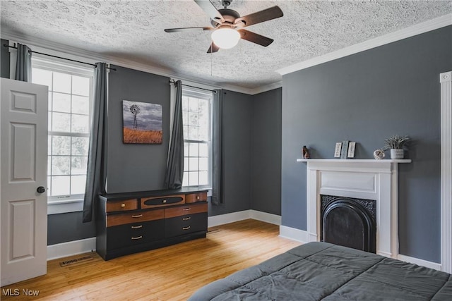bedroom featuring a textured ceiling, light wood-style flooring, baseboards, ornamental molding, and a fireplace