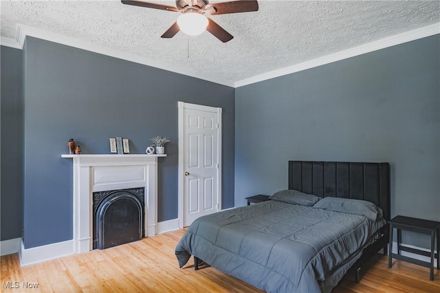 bedroom featuring wood finished floors, a textured ceiling, baseboards, ornamental molding, and a fireplace