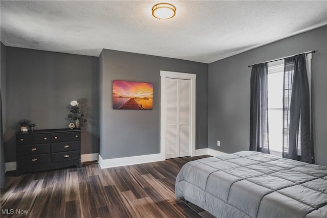 bedroom featuring baseboards, dark wood-style floors, a closet, and a textured ceiling