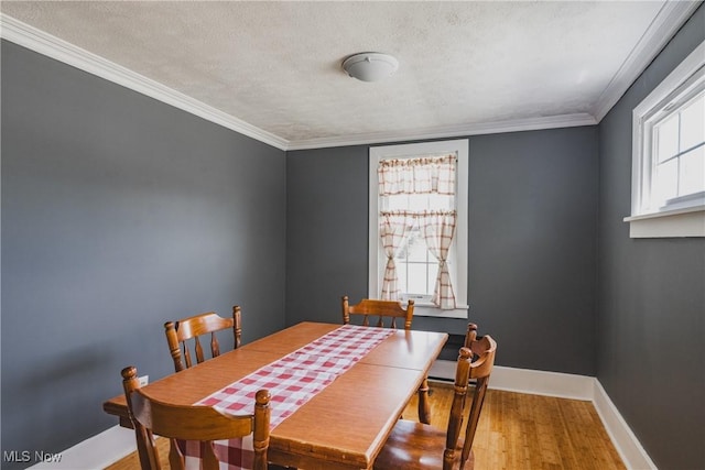 dining area featuring wood finished floors, baseboards, a textured ceiling, and crown molding
