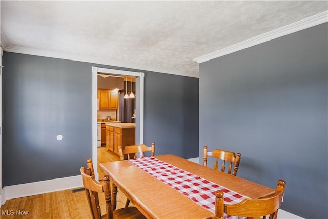 dining room with light wood-type flooring, ornamental molding, a textured ceiling, and baseboards