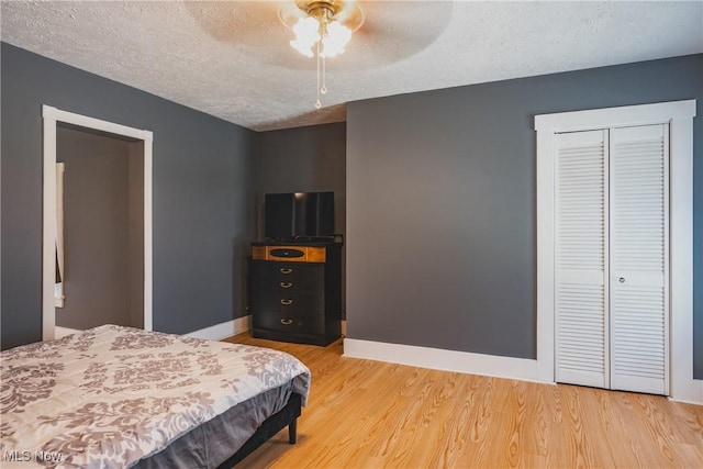 bedroom with a textured ceiling, light wood-style flooring, a closet, baseboards, and a ceiling fan