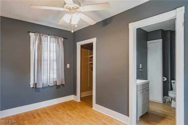 unfurnished bedroom featuring light wood-style floors, baseboards, a spacious closet, and ceiling fan