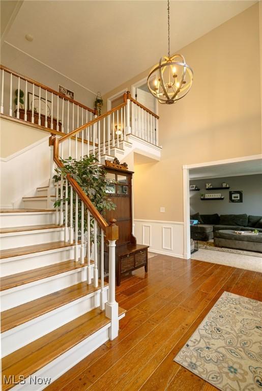 20686 Wildwood Ln, Strongsville, OH 44149 - stairway featuring a chandelier, wainscoting, wood-type flooring, a decorative wall, and a high ceiling