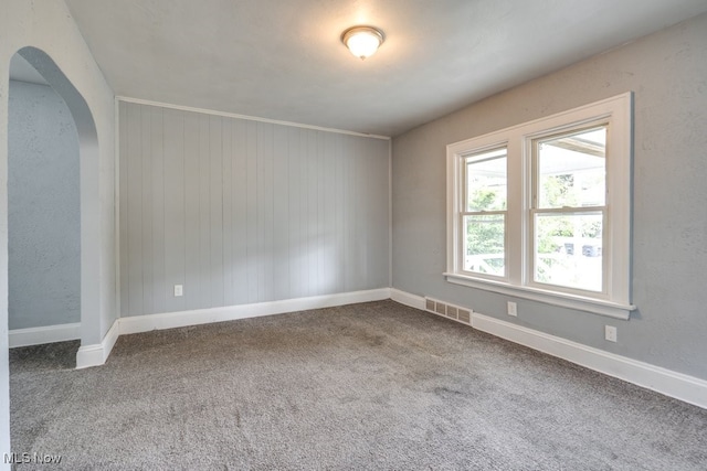 1866 17th St SW, Akron, OH 44314 - carpeted empty room with baseboards, arched walkways, and wood walls