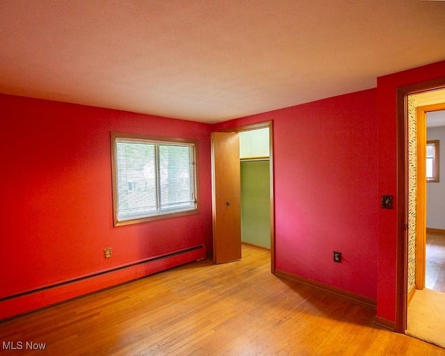 433 University Ave, Elyria, OH 44035 - unfurnished bedroom featuring baseboard heating, light wood-style floors, a closet, and a spacious closet