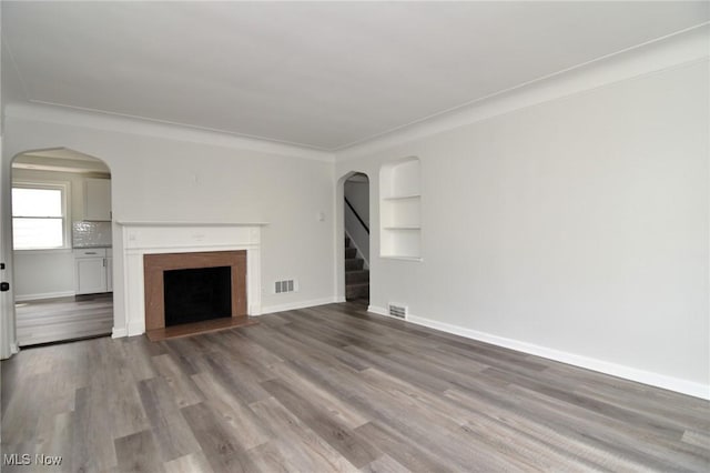 3890 Grosvenor Rd, South Euclid, OH 44118 - unfurnished living room with arched walkways, wood finished floors, a fireplace, baseboards, and built in shelves