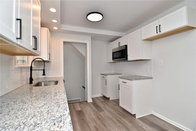 3890 Grosvenor Rd, South Euclid, OH 44118 - kitchen with a sink, stainless steel microwave, light stone countertops, backsplash, and light wood-type flooring