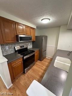4757 Ledgewood Dr Unit 7-A, Medina, OH 44256 - kitchen featuring appliances with stainless steel finishes, a sink, light wood-style flooring, brown cabinetry, and backsplash