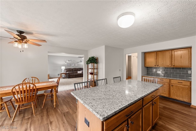 8373 Forest View Dr, Olmsted Falls, OH 44138 - kitchen with wood finished floors, decorative backsplash, ceiling fan, a center island, and light stone counters