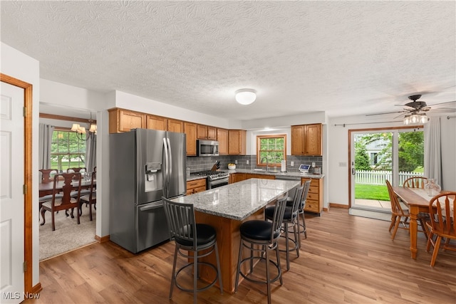 8373 Forest View Dr, Olmsted Falls, OH 44138 - kitchen featuring appliances with stainless steel finishes, light wood-style flooring, a sink, brown cabinetry, and a kitchen breakfast bar