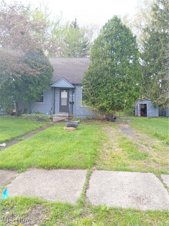 702 Hall St NW, Warren, OH 44483 - view of front of property featuring a front yard, a shingled roof, and an outbuilding