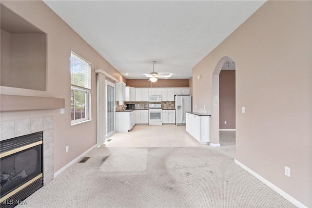7284 Forest Cove Ln, Northfield, OH 44067 - unfurnished living room featuring baseboards, light colored carpet, a tiled fireplace, ceiling fan, and arched walkways
