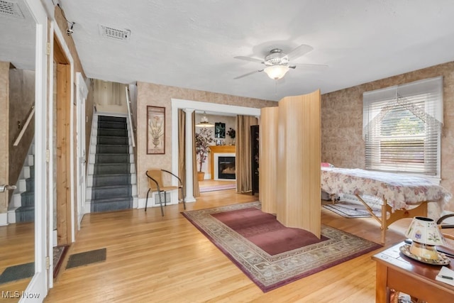 7285 Center St, Mentor, OH 44060 - living area featuring wood finished floors, wallpapered walls, stairway, a fireplace, and a ceiling fan